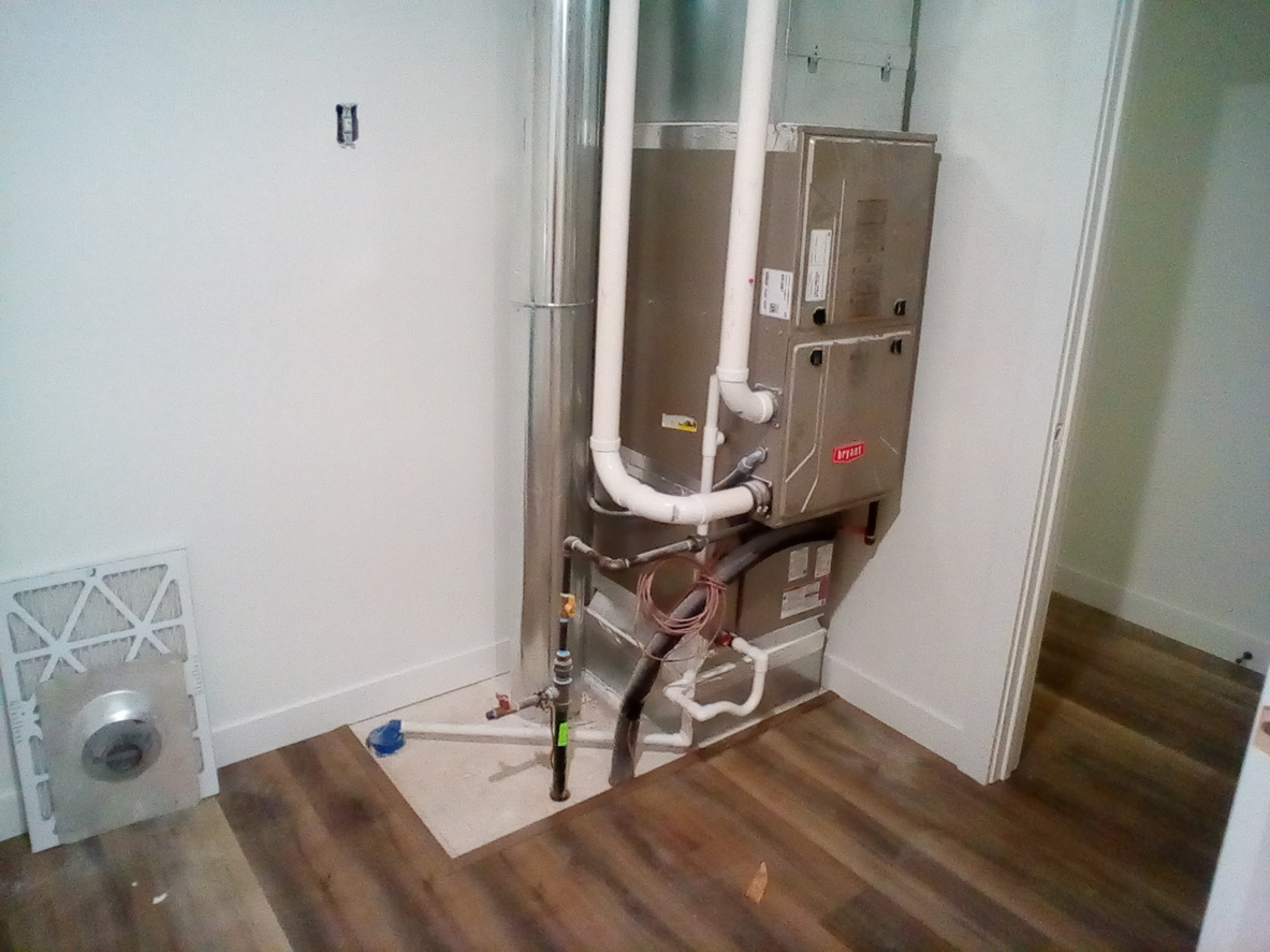 A residential HVAC system installed in a small closet, showing a metal furnace unit.