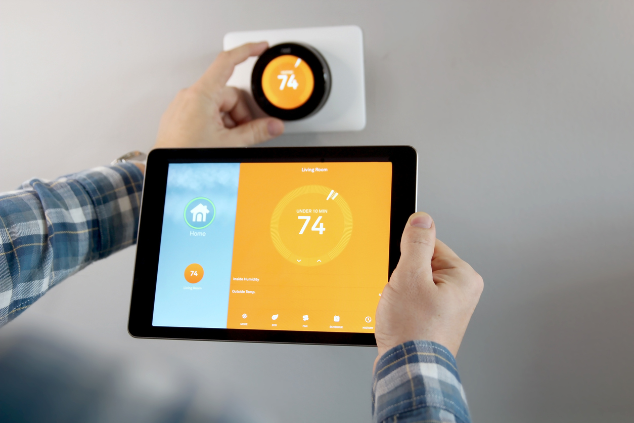 A man adjusts the temperature on a smart thermostat using a tablet with a smart home app in a modern living room.