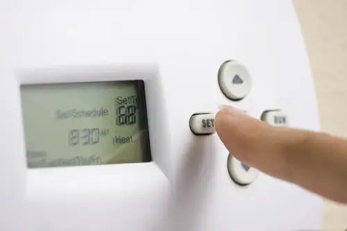 Female hand setting thermostat to 68 degrees Fahrenheit to save energy in the winter.