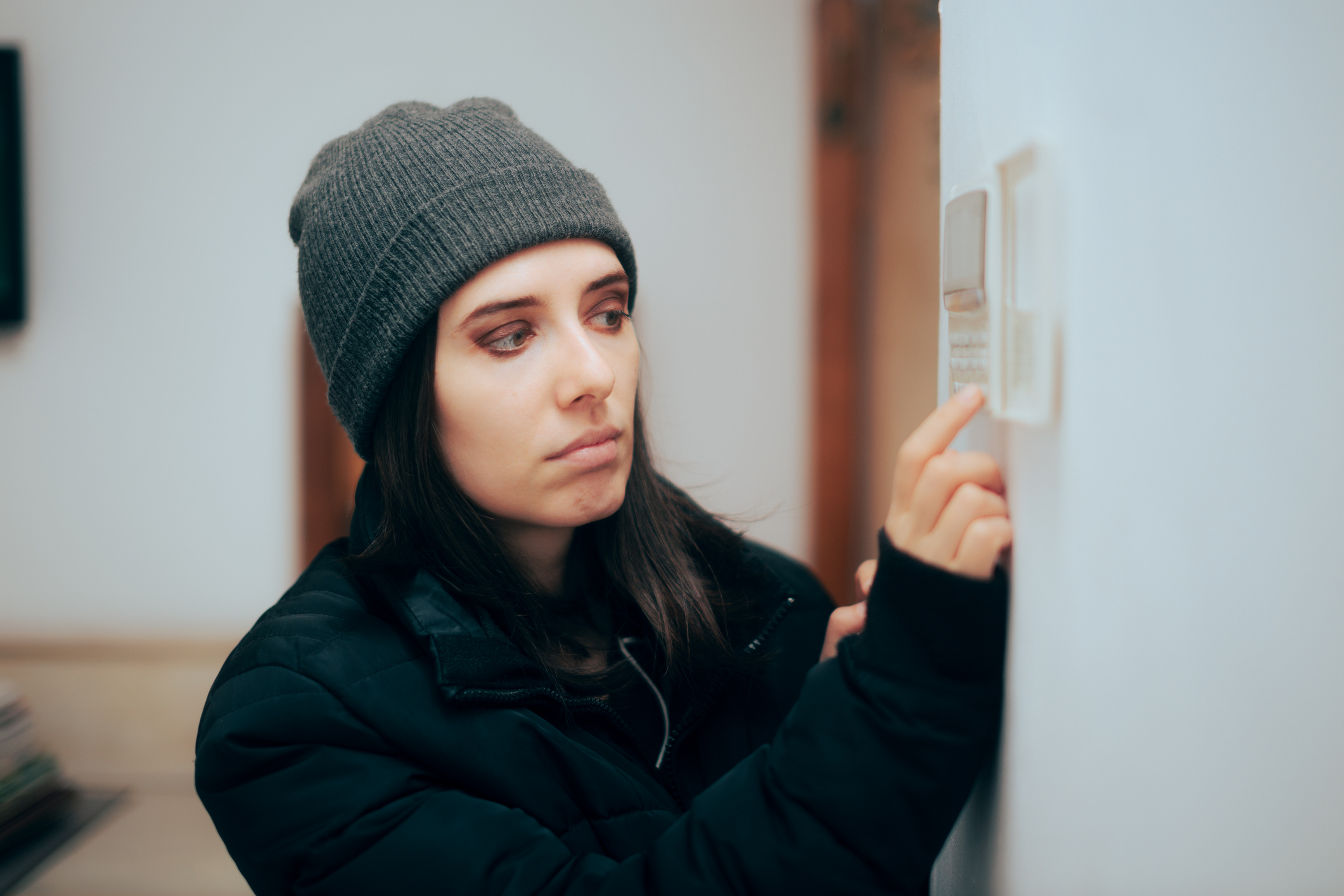 A woman who appears cold setting her thermostat.